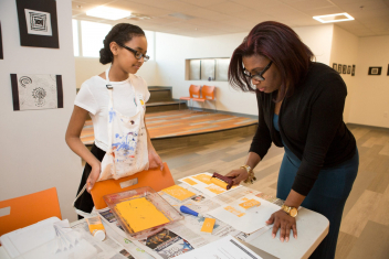 Middle school girl print making A middle school student watches as a teacher practices a print-making technique she demonstrated for her.